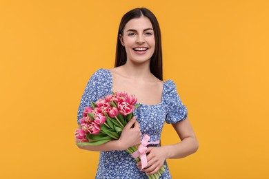 Happy young woman with beautiful bouquet on orange background