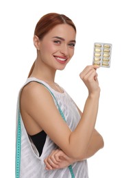 Happy young woman with pills and measuring tape on white background. Weight loss