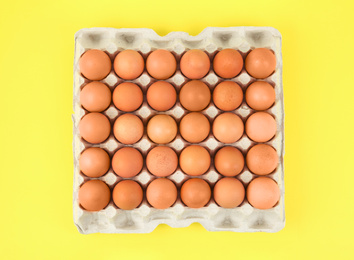 Raw chicken eggs on yellow background, top view