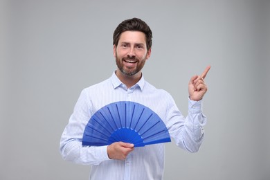 Photo of Happy man holding hand fan on light grey background