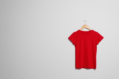 Photo of Hanger with red t-shirt on light wall. Mockup for design