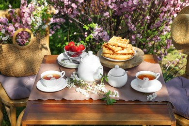 Photo of Beautiful spring flowers, freshly baked waffles and ripe strawberries on table served for tea drinking in garden