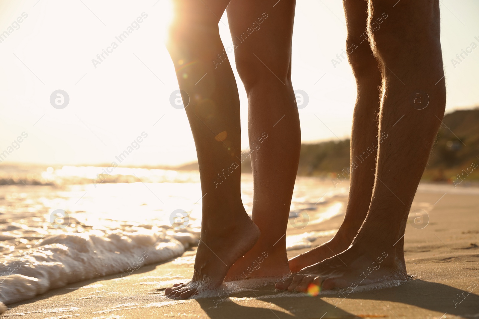 Photo of Couple on sandy beach near sea at sunset, closeup of legs