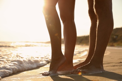 Couple on sandy beach near sea at sunset, closeup of legs