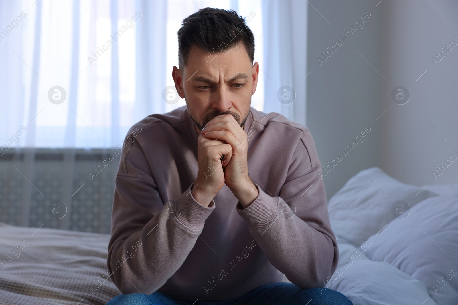 Photo of Upset man sitting on bed at home. Loneliness concept