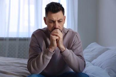 Photo of Upset man sitting on bed at home. Loneliness concept