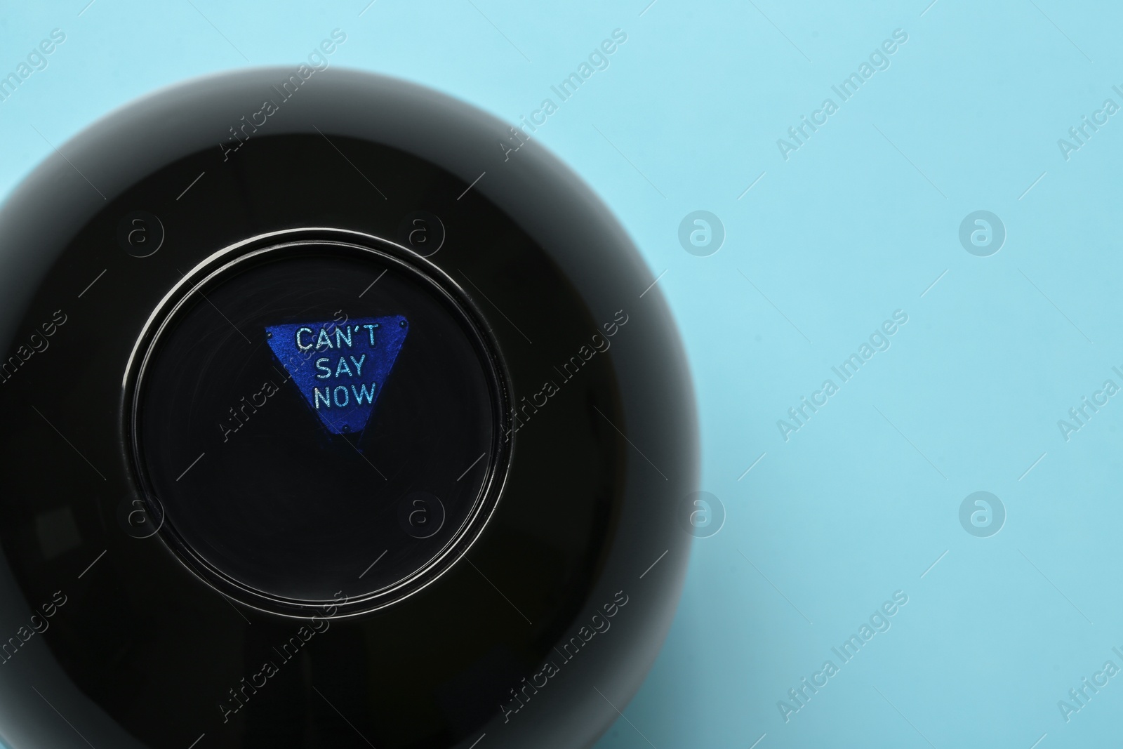 Photo of Magic eight ball with prediction Can't Say Now on light blue background, top view. Space for text