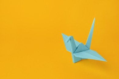 Photo of Origami art. Beautiful light blue paper crane on orange background, space for text