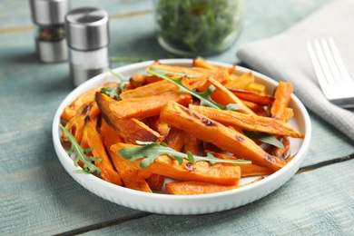 Photo of Plate with baked sweet potato slices and arugula on wooden table