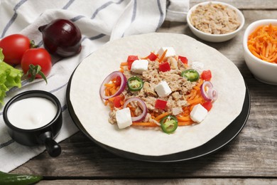 Photo of Delicious tortilla with tuna, vegetables and cheese on wooden table. Cooking shawarma