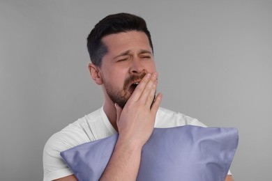 Photo of Sleepy man with pillow yawning on grey background. Insomnia problem