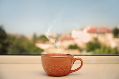 Image of Cup of hot coffee on window sill indoors