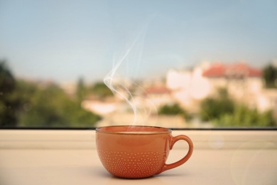 Cup of hot coffee on window sill indoors