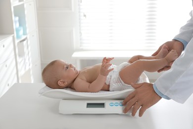 Pediatrician weighting cute baby in clinic, closeup. Health care