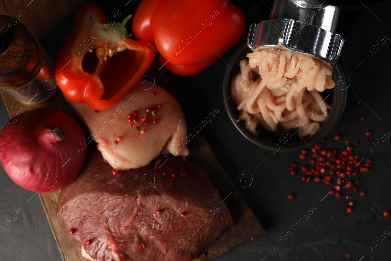 Photo of Electric meat grinder with chicken mince and products on black table, flat lay