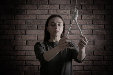 Image of Depressed woman with rope noose near brick wall. Suicide concept