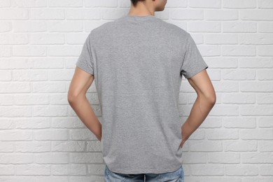 Photo of Man wearing gray t-shirt near white brick wall, back view. Mockup for design