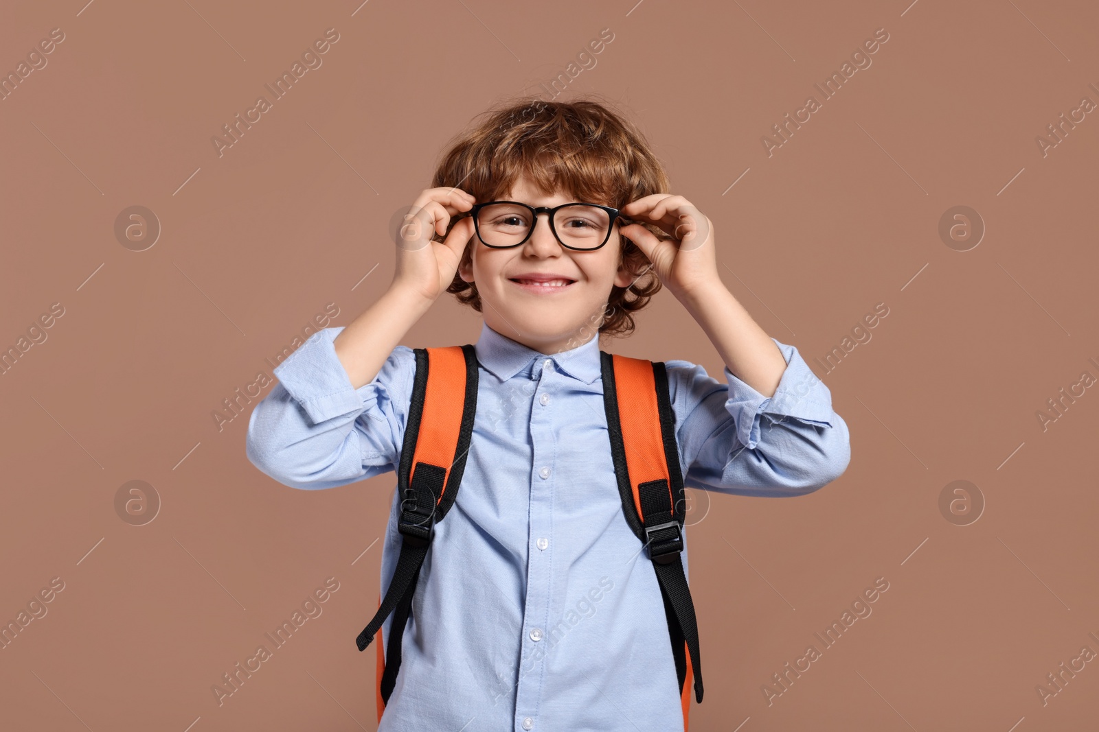 Photo of Happy schoolboy in glasses with backpack on brown background