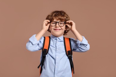 Happy schoolboy in glasses with backpack on brown background