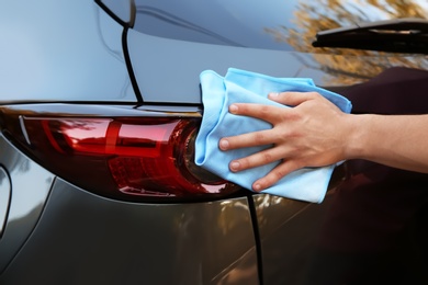 Photo of Young man washing car rear light with rag, closeup