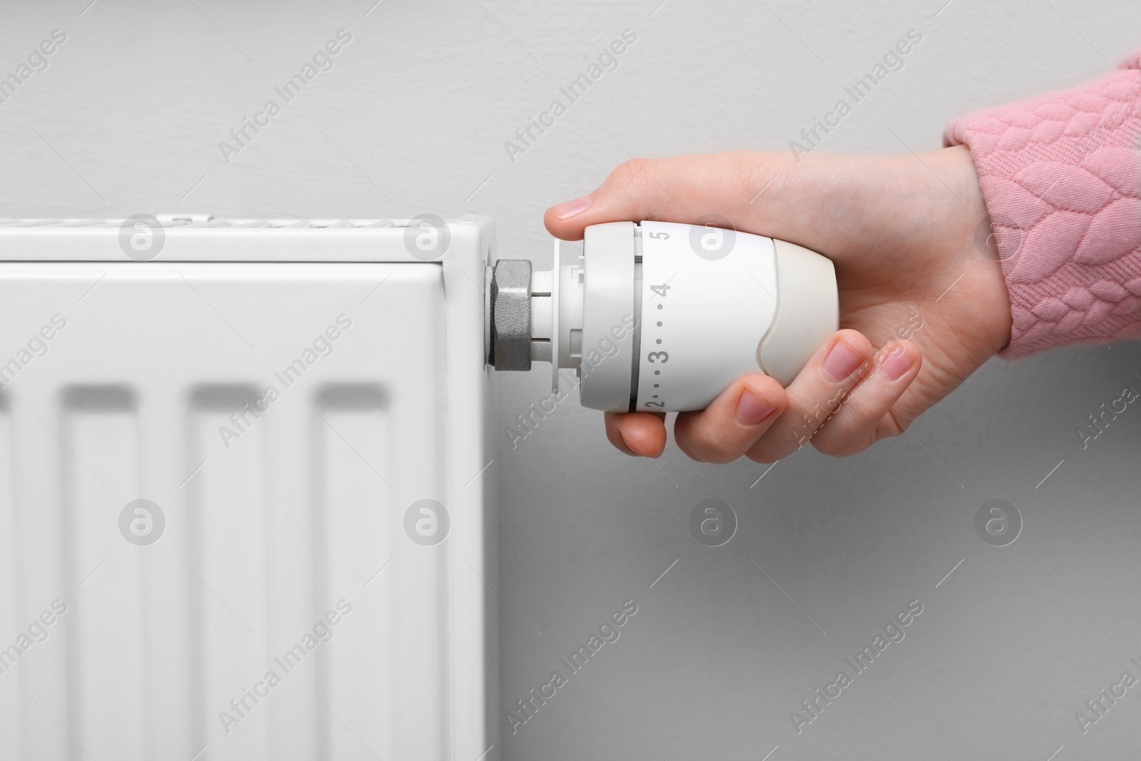 Photo of Girl adjusting heating radiator thermostat near white wall indoors, closeup