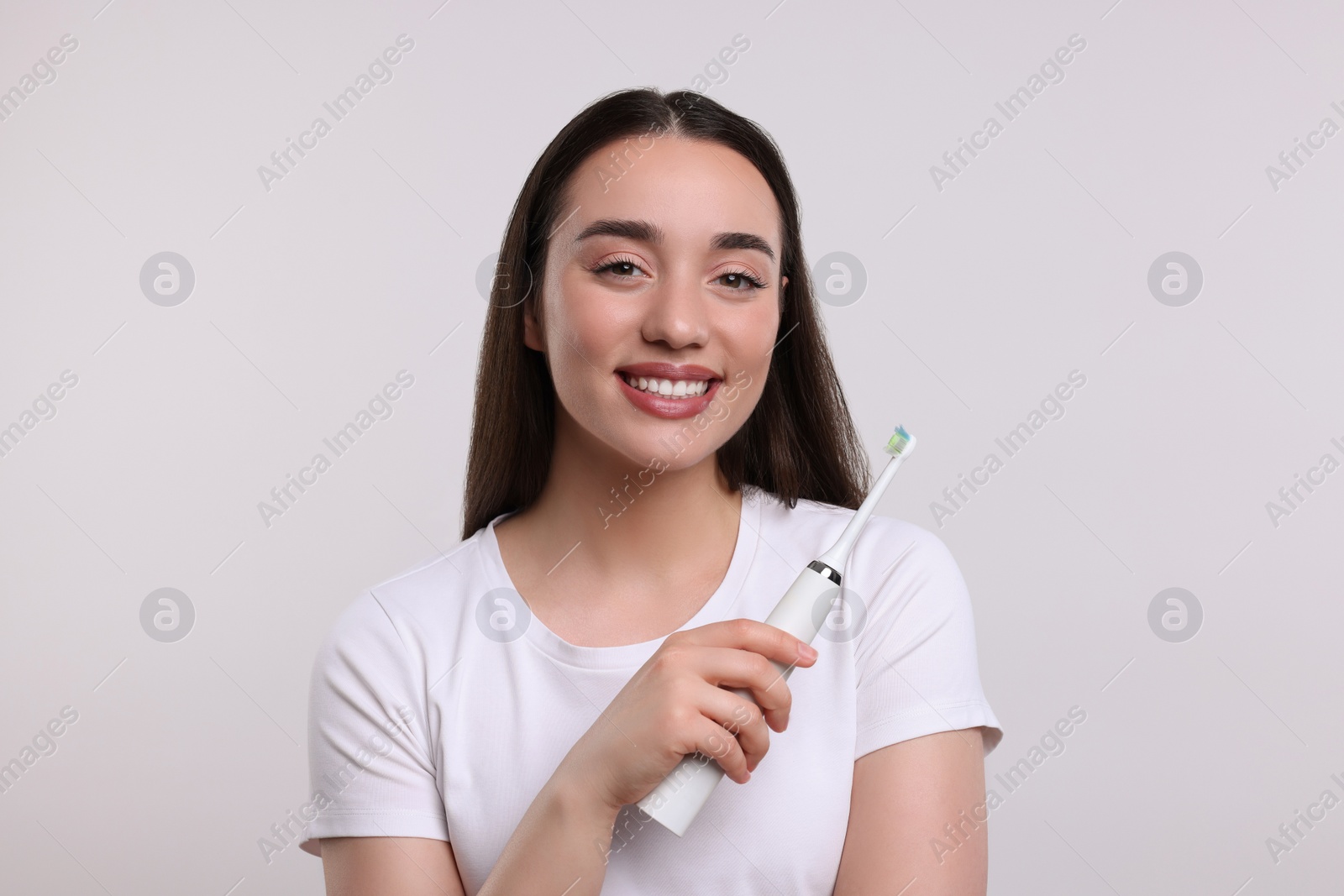 Photo of Happy young woman holding electric toothbrush on white background