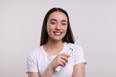 Photo of Happy young woman holding electric toothbrush on white background