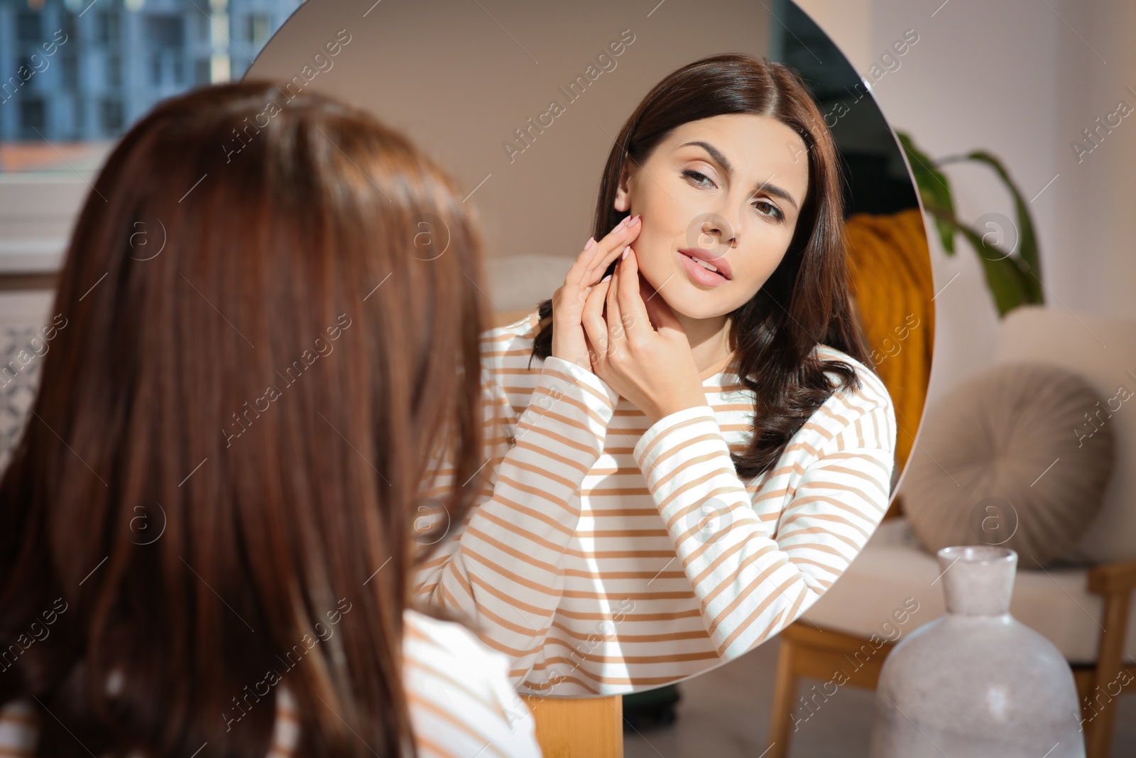 Photo of Young woman looking in mirror and squeezing pimple indoors. Hormonal disorders