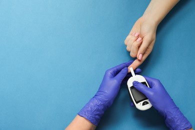 Photo of Diabetes. Doctor checking patient's blood sugar level with glucometer on blue background, top view. Space for text