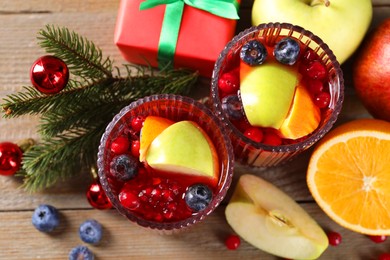 Photo of Aromatic Sangria drink in glasses, ingredients and Christmas decor on wooden table, flat lay