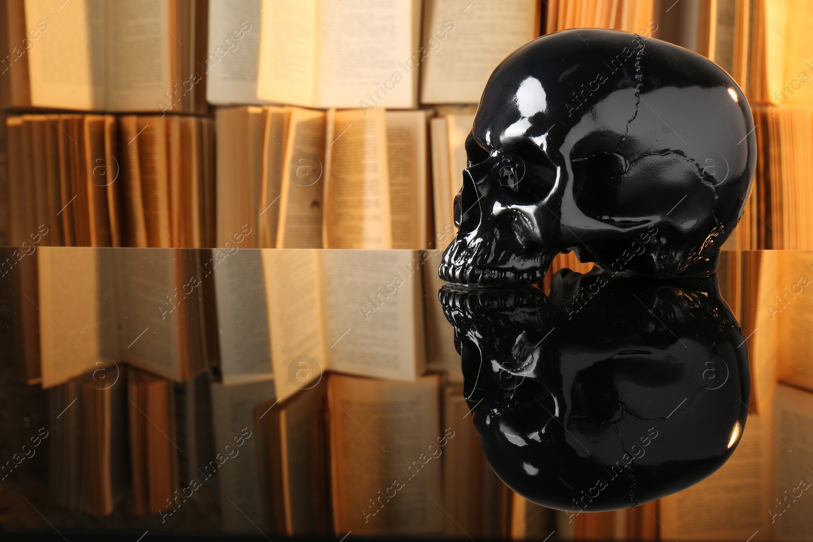 Photo of Black human skull on mirror table near books. Space for text