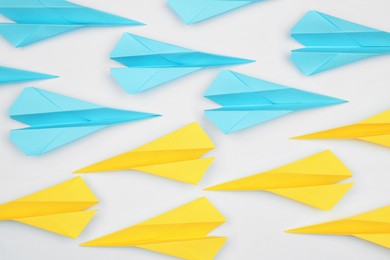 Handmade paper planes in light blue and yellow colors on white table, flat lay