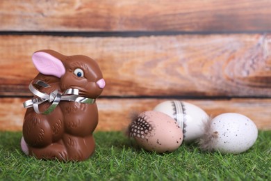 Photo of Easter celebration. Cute chocolate bunny and painted eggs on grass against wooden background. Space for text