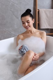 Woman taking bath with mesh pouf indoors