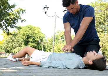 Photo of Man performing CPR on unconscious young woman outdoors. First aid