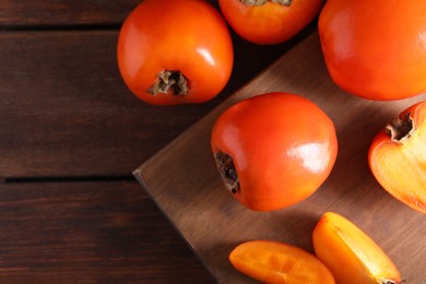 Photo of Delicious ripe persimmons on wooden table, top view. Space for text