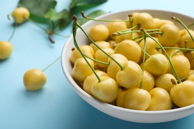 Bowl with ripe yellow cherries on turquoise background, closeup