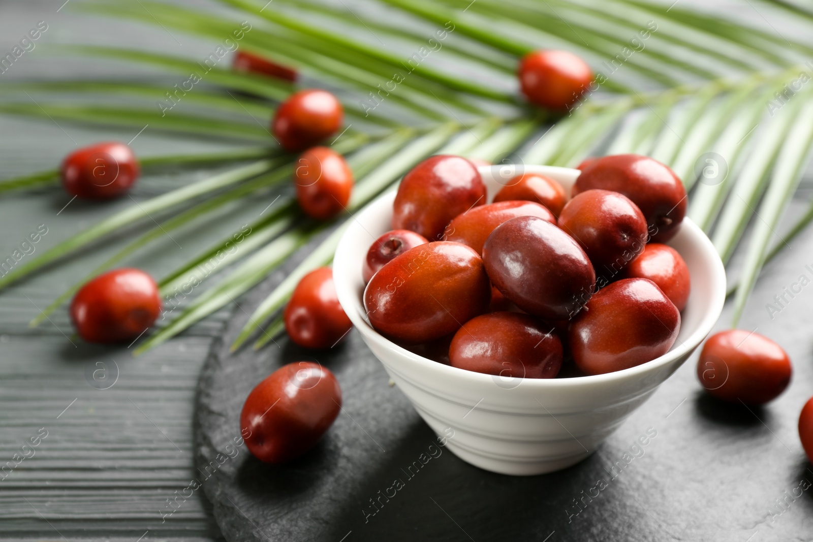 Photo of Palm oil fruits in bowl on grey wooden table, closeup