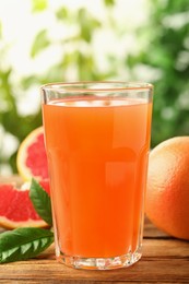 Photo of Glass of delicious grapefruit juice on wooden table against blurred background