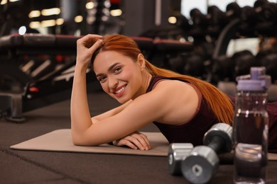 Happy young woman lying on mat in gym