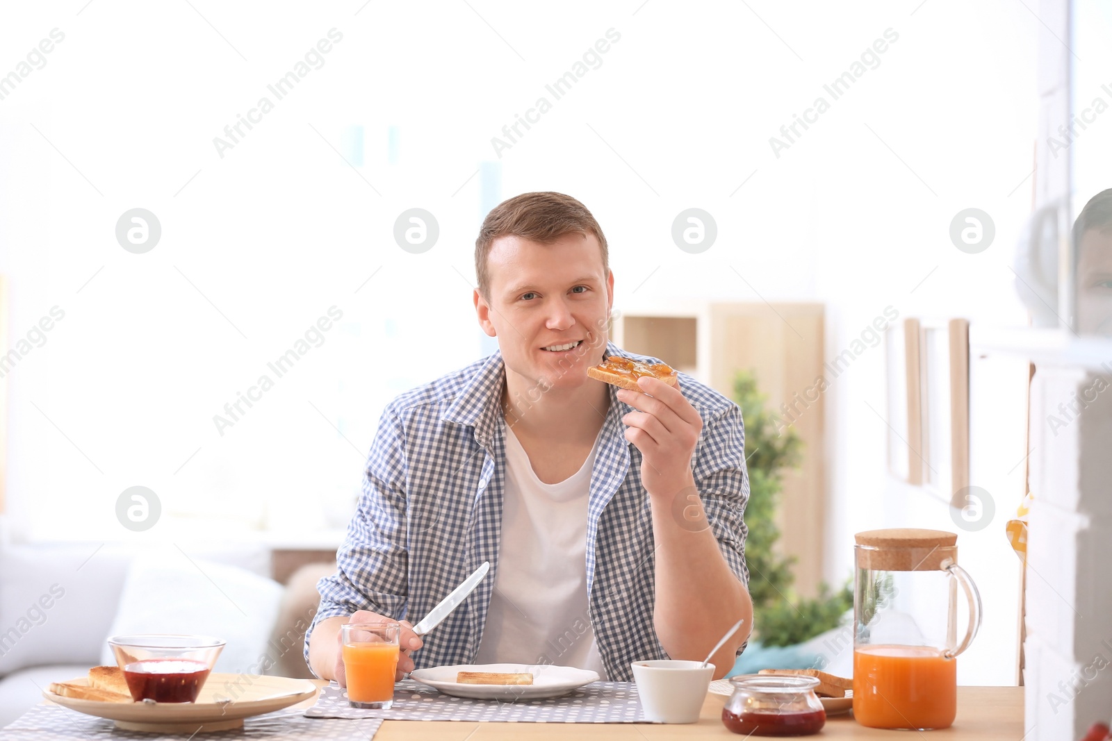 Photo of Young man eating tasty toasted bread with jam at table