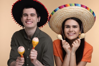 Photo of Lovely couple woman in Mexican sombrero hats with maracas on beige background