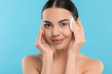 Photo of Beautiful woman removing makeup with cotton pads on light blue background