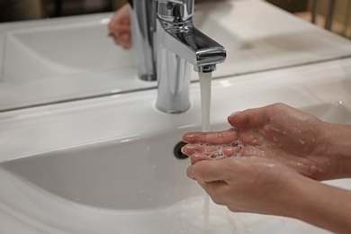 Photo of Woman washing hands under tap indoors, closeup