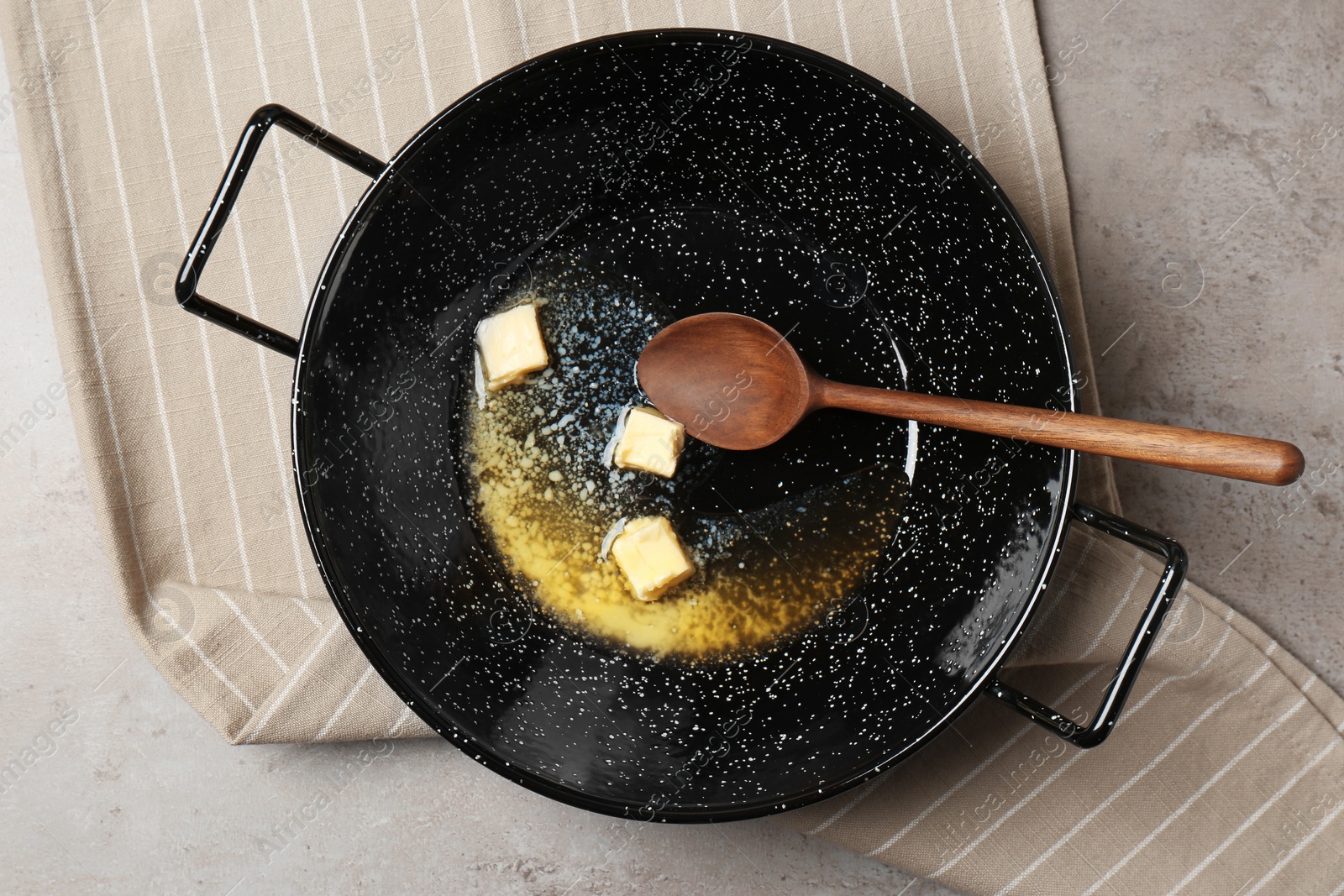 Photo of Frying pan with melting butter and spoon on grey table, top view