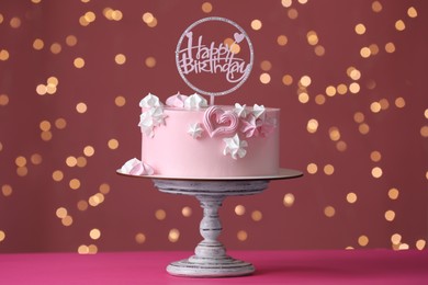 Photo of Beautifully decorated birthday cake on pink table against blurred festive lights
