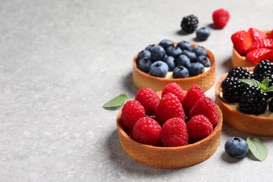 Photo of Tartlets with different fresh berries on light grey table, space for text. Delicious dessert
