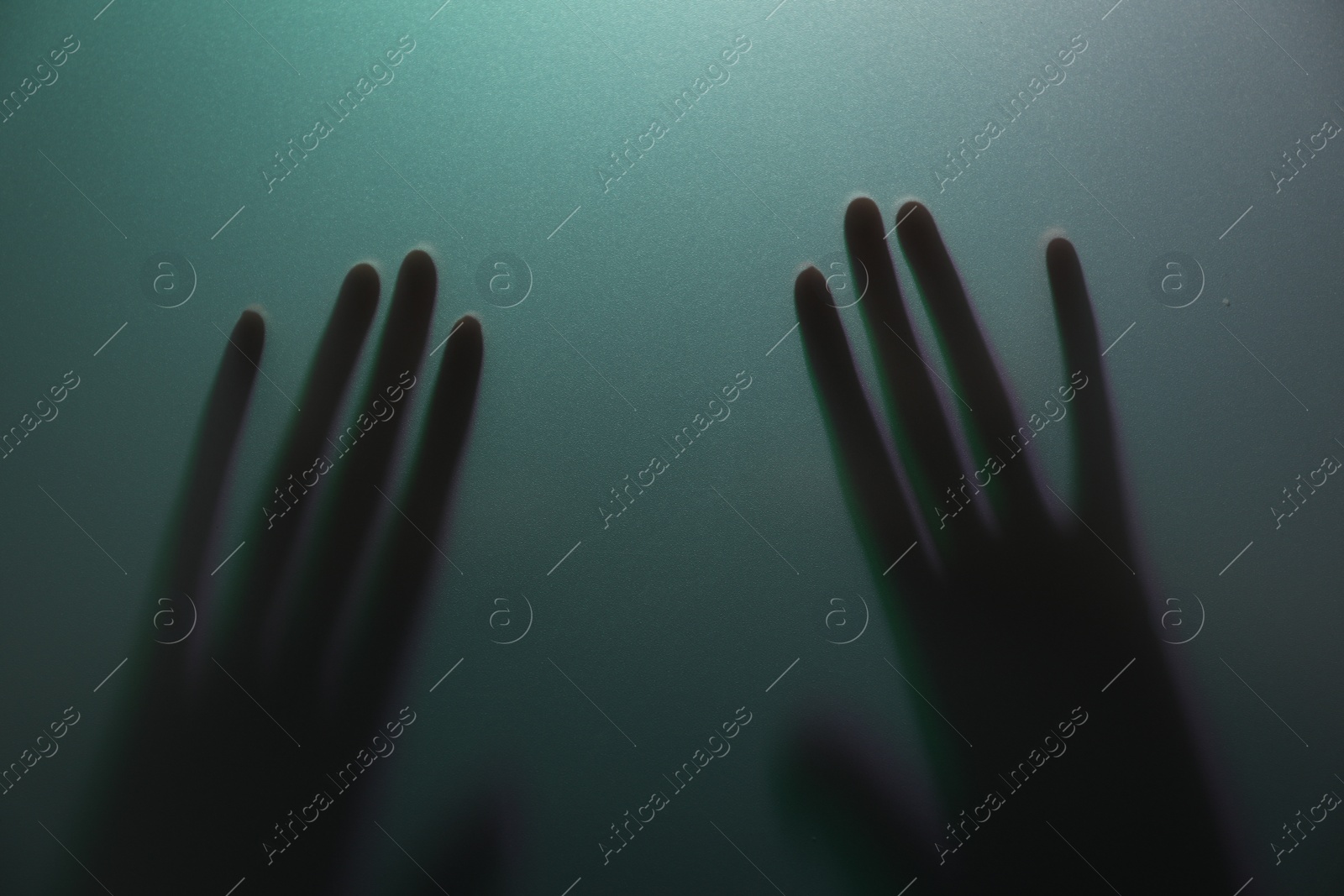 Photo of Silhouette of creepy ghost behind glass against color background, closeup
