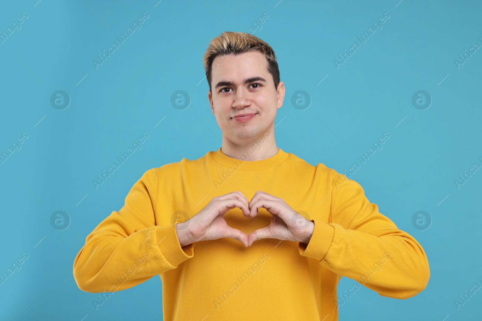 Photo of Young man showing heart gesture with hands on light blue background