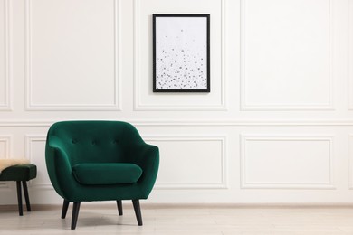 Photo of Comfortable armchair and picture on white wall indoors. Space for text
